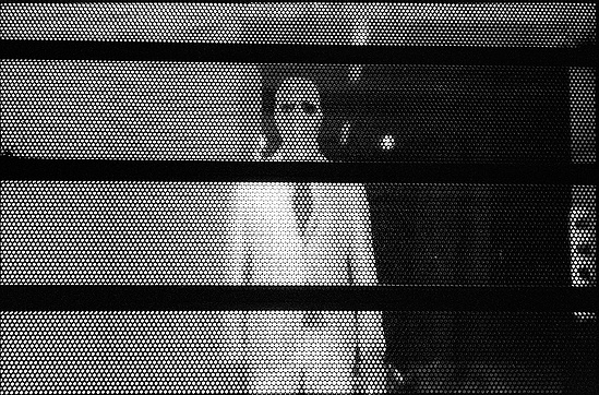 Nigredo: a figure behind a perforated screen